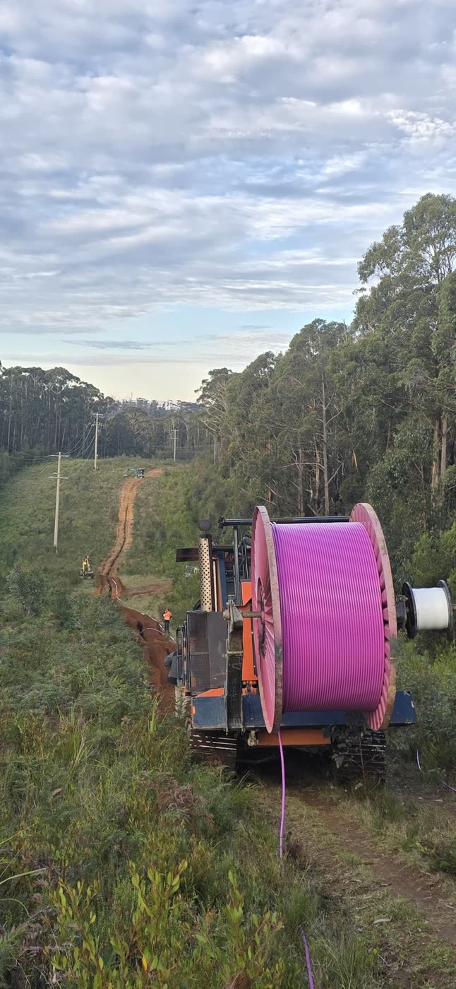 CFH Civils trencher hauling a fibre optic cable drum along a rural utility corridor at dusk